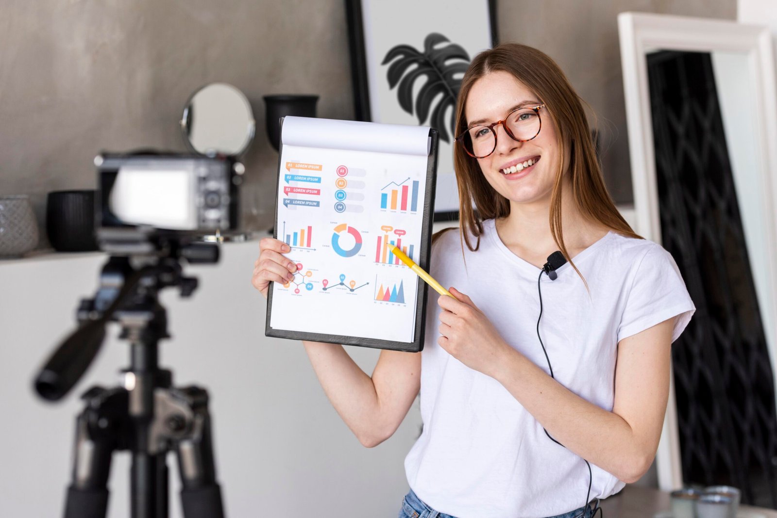 Young female content creator filming a tutorial on video marketing for beginners, smiling while holding a clipboard with colorful charts and graphs in front of a professional camera setup.