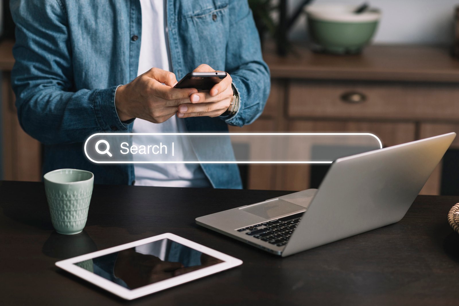 A person using a smartphone while sitting at a desk with a laptop and tablet, representing the concept of online search and digital marketing. This image is ideal for illustrating topics like Google Ads retargeting, where user behavior is tracked across devices to deliver targeted ads.